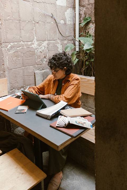 leticia sentada dentro da cafeteria, com o tablet, enquanto trabalha em seus projetos, da sua própria empresa'