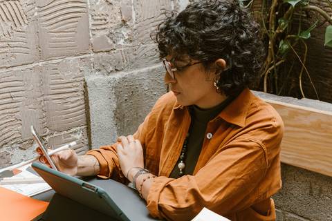 leticia sentada dentro da cafeteria, com o tablet, olhando para seu celular de trabalho'