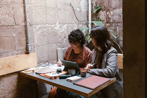 le e ni juntas na foto, sentadas na mesa, enquanto olham seu tablet'