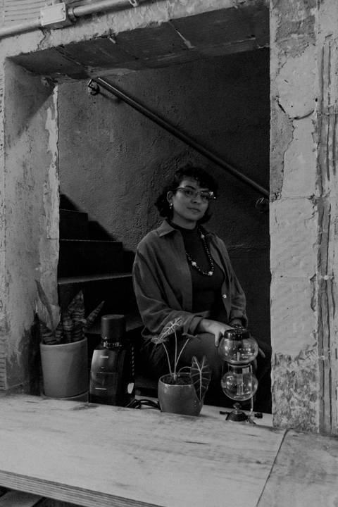 leticia sentada dentro da cafeteria, na escadaria, olhando para a câmera'