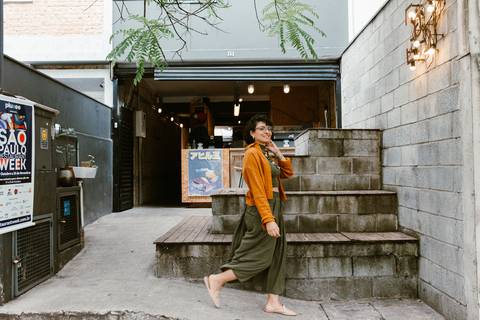 leticia na parte de fora da cafeteria em frente a escadaria, caminhando em frente a cafeteria'