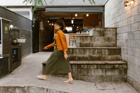 leticia na parte de fora da cafeteria em frente a escadaria, caminhando agora para o outro lado da rua '