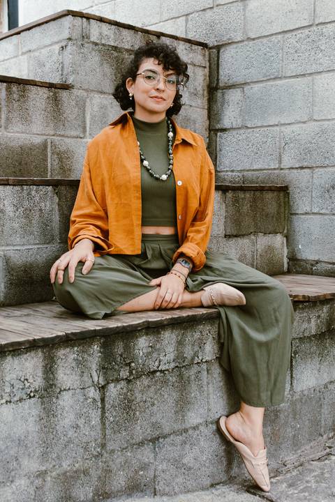 leticia sentada na escadaria em frente a cafeteria, com uma das pernas cruzadas'