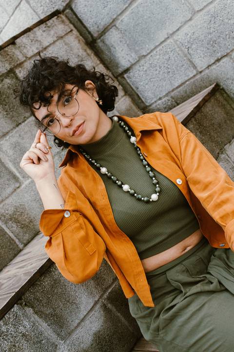 leticia sentada na escadaria em frente a cafeteria, com a mão segurando o seu óculos em seu rosto'