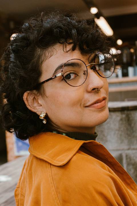 leticia em pé na escadaria em frente a cafeteria,  olhando por cima dos ombros, de costas, seu rosto enquadrado na foto'