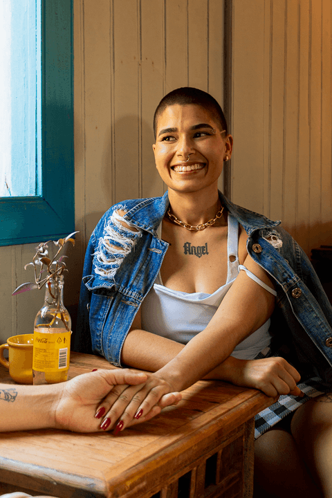 mika sentada na cadeira em frente a mesa de madeira, sorrindo ao olhar para a le'