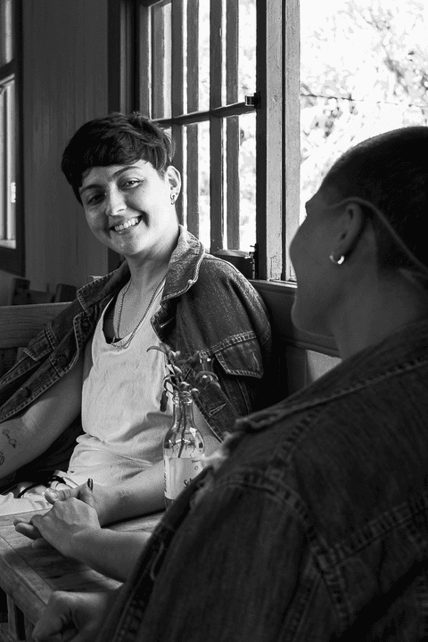 le sentada na cadeira em frente a mesa de madeira, sorrindo ao olhar para a mika'