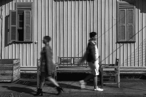 mika e le andando em frente aos bancos de madeira da cafeteria, elas estão de costas uma para a outra'