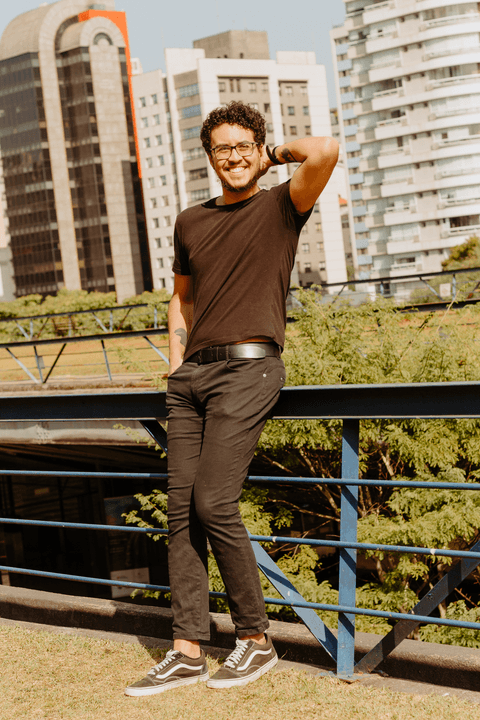 Leo no centro cultural são paulo, em pé escontado no corrimão, com uma das mãos na cabeça, sorrindo'