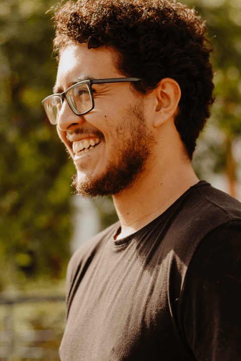 Leo no centro cultural são paulo, sorrindo, com o enquadramento mais fechado em seu rosto, fundo verde'