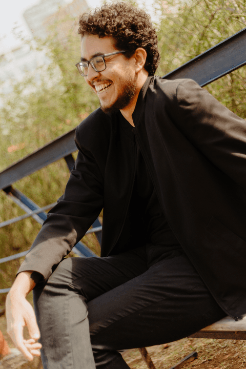 Leo no centro cultural são paulo, sentado no banco, sorrindo'