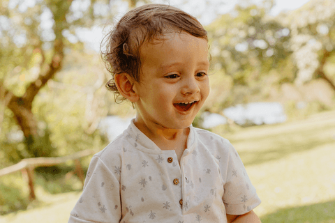 lorenzo sorrindo encantado com a brincadeira, lago e vegetação ao fundo'