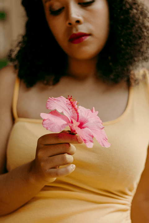 leticia com a flor em sua mão olhando para ela, mais parte do seu rosto aparecendo'