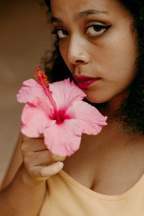leticia com a flor em sua mão olhando para ela, flor bem próxima ao seu rosto enquanto olha para a câmera'