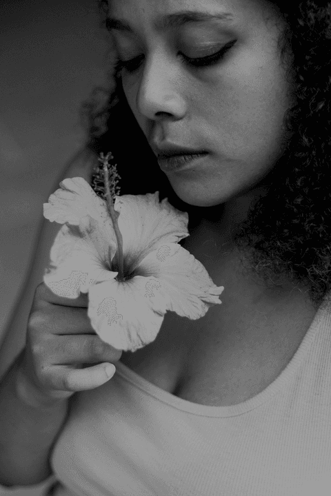 leticia com a flor em sua mão olhando para ela, cheirando e flor, foto em preto e branco'
