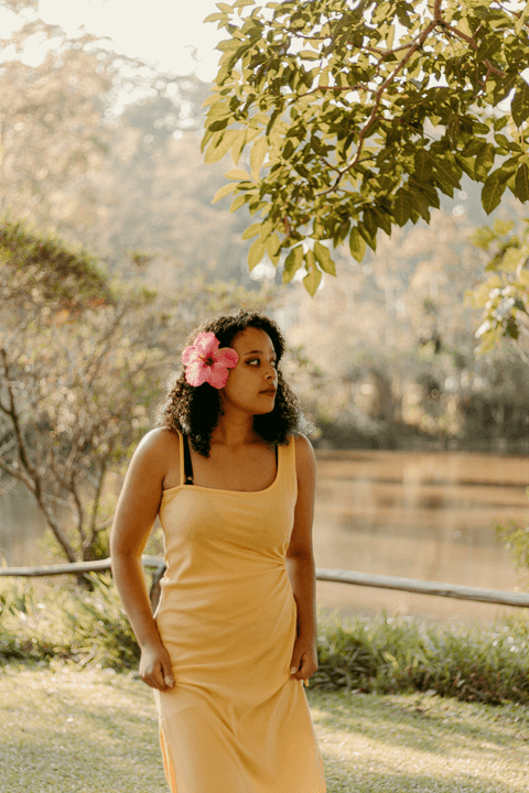 leticia mais próxima de mim, em meio as vegetaçõs do parque e o lago ao fundo, caminhando, com flor rosa na cabeça'