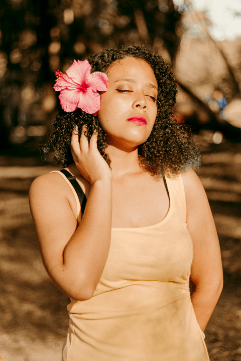 leticia com uma mão somente no cabelo ao lado da flor rosa'