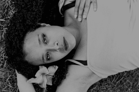 leticia deitada na grama, com uma mão atrás da cabeça e outra sobre o peito, foto em preto e branco'