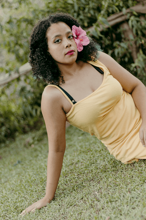 leticia sentada na grama, com uma mão sobre o corpo e outra na grama'