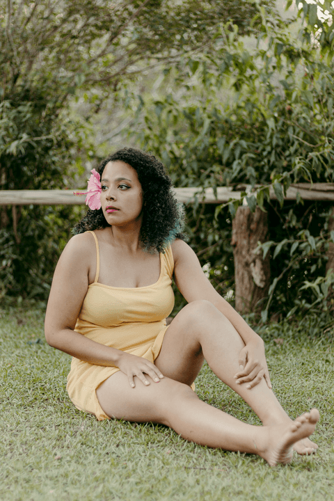leticia sentada na grama, com as mãos sobre o corpo, olhando além'