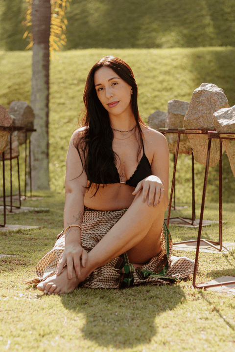 luiza sentada em meio as pedras artísticas do sec itaquera, com as pernas cruzadas, mão sobre as pernas, sorriso leve'