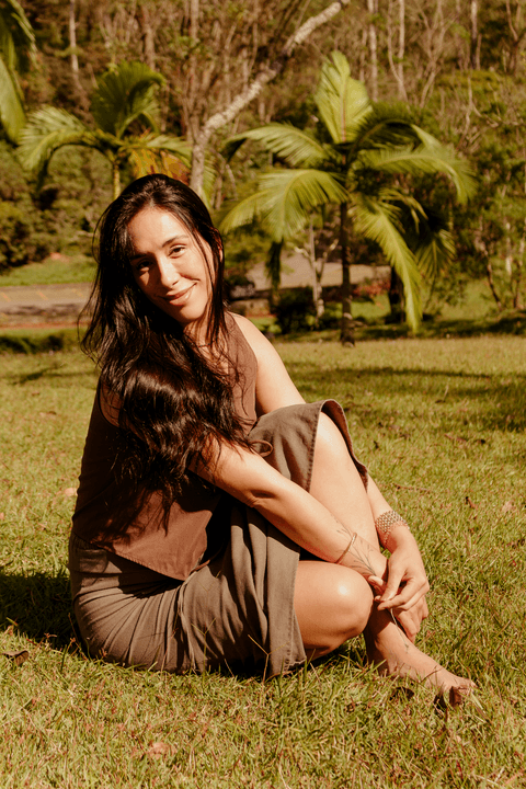 luiza sentada no mato, campo aberto no sesc itaquera, abraçando suas pernas enquanto sorri de leve para mim, cabelos longos soltos'