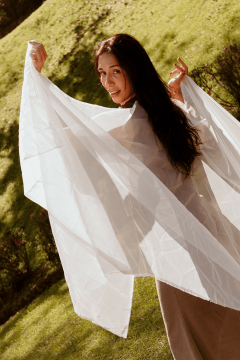 luiza bailando pelo campo de grama com um tecido branco transparente, sorrindo'