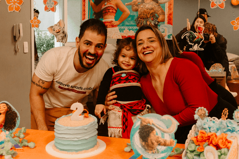 os pais de maria eduarda com ela em frente ao bolo na hora do parabéns, todos sorrindo'