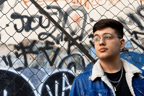 nathan encostado na grade olhando para o horizonte, grafites ao fundo'
