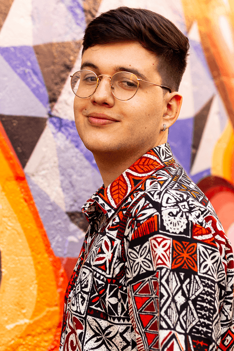 nathan olhando para a câmera, com sorriso leve em seu rosto, fundo de parede colorido'