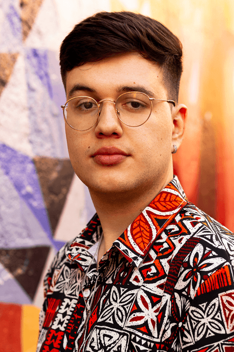 nathan olhando para a câmera, sério, fundo de parede colorido, mais de frente para mim, usando óculos'