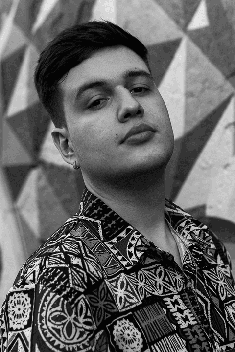 nathan olhando para a câmera, sério, fundo de parede colorido, mais de frente para mim, sem óculos, foto em preto e branco'