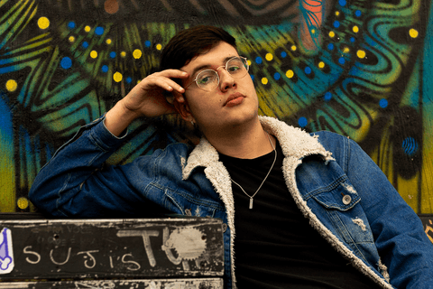 nathan sentado, apoiado com o cotovelo em uma estrutura de concreto, olhando para mim, com óculos'