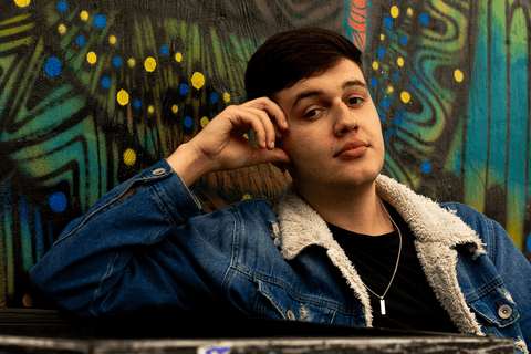 nathan sentado, apoiado com o cotovelo em uma estrutura de concreto, olhando para mim, sem óculos'