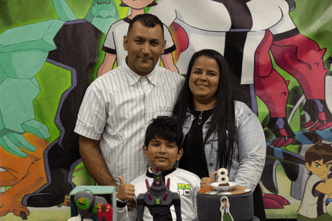 pedro com seus pais na mesa de decoração e do bolo, juntos, sorrindo, final da festa'