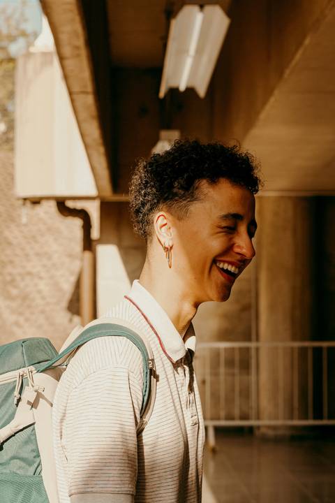 raoni com meio rosto sendo iluminado pela luz do sol, sorrindo, com os olhos fechados, com o corpo inclinado para a frente'