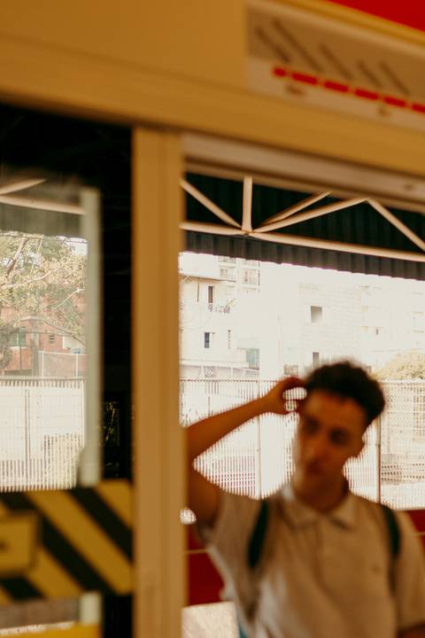 raoni encostado na porta de segurança do metrô, levemente desfocado'