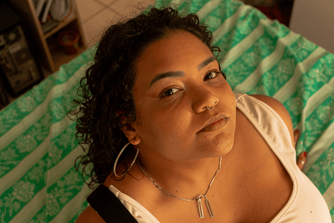 suelen semi deitada em sua cama, ângulo por cima, ela olha para a câmera, fundo de lençol verde'
