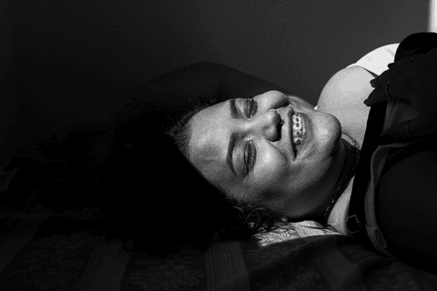 suelen deitada em sua cama, olhando para mim, luz do sol batendo em parte do seu rosto, sorrindo com os olhos fechados'