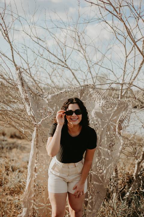 ensaio feminino externo com arvores e oculos escuro sorrindo'