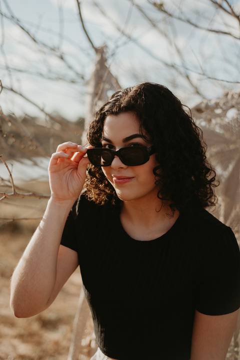ensaio feminino externo com arvores e oculos escuro sorrindo'