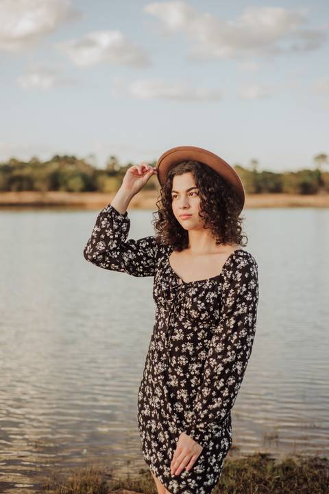 ensaio feminino externo a beira do lago com roupa preta e branca e chapeu marron estilo boho, menina cacheada'
