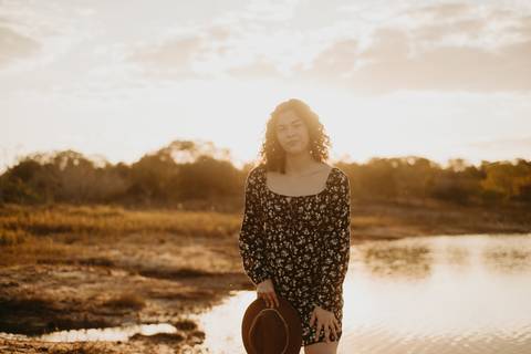 ensaio feminino externo a beira do lago com roupa preta e branca e chapeu marron estilo boho, menina cacheada. fotos no por do sol, '
