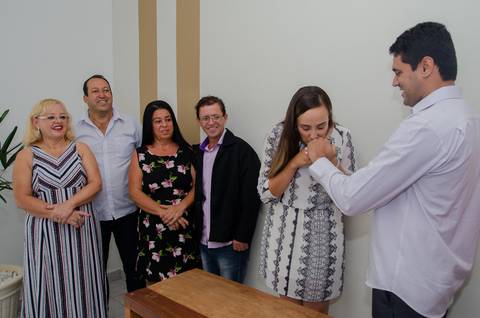 sob o olhar atento dos pais, noiva, nova esposa, beija aliança na mão do marido'