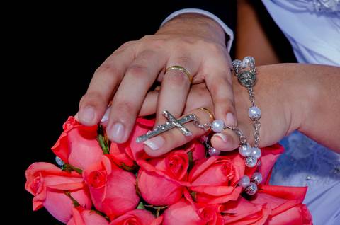 Bruna e Osvaldo. Mãos unidas sobre um arranjo de flores do casamento'