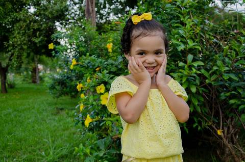Ensaio pré aniversário de 03 anos - Nicole - Criança de 03 anos em sessão fotográfica com as mãos no rosto e sorrindo naturalmente'