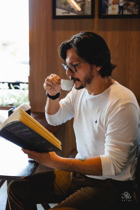 Modelo lendo um livro e tomando um café'