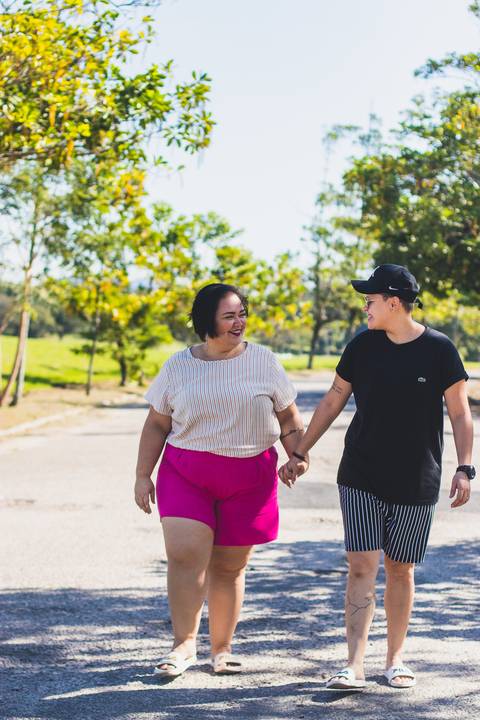 casal anda de mãos dadas em estrada verde se olhando '