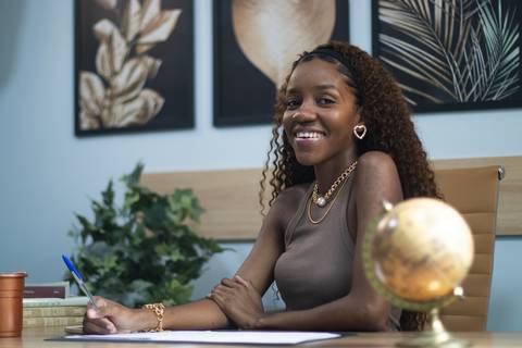 mulher negra segura caneta em mesa de escritório olhando para a câmera'