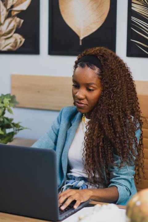 menina negra empresária olha para notebook sentada em mesa de escritório'